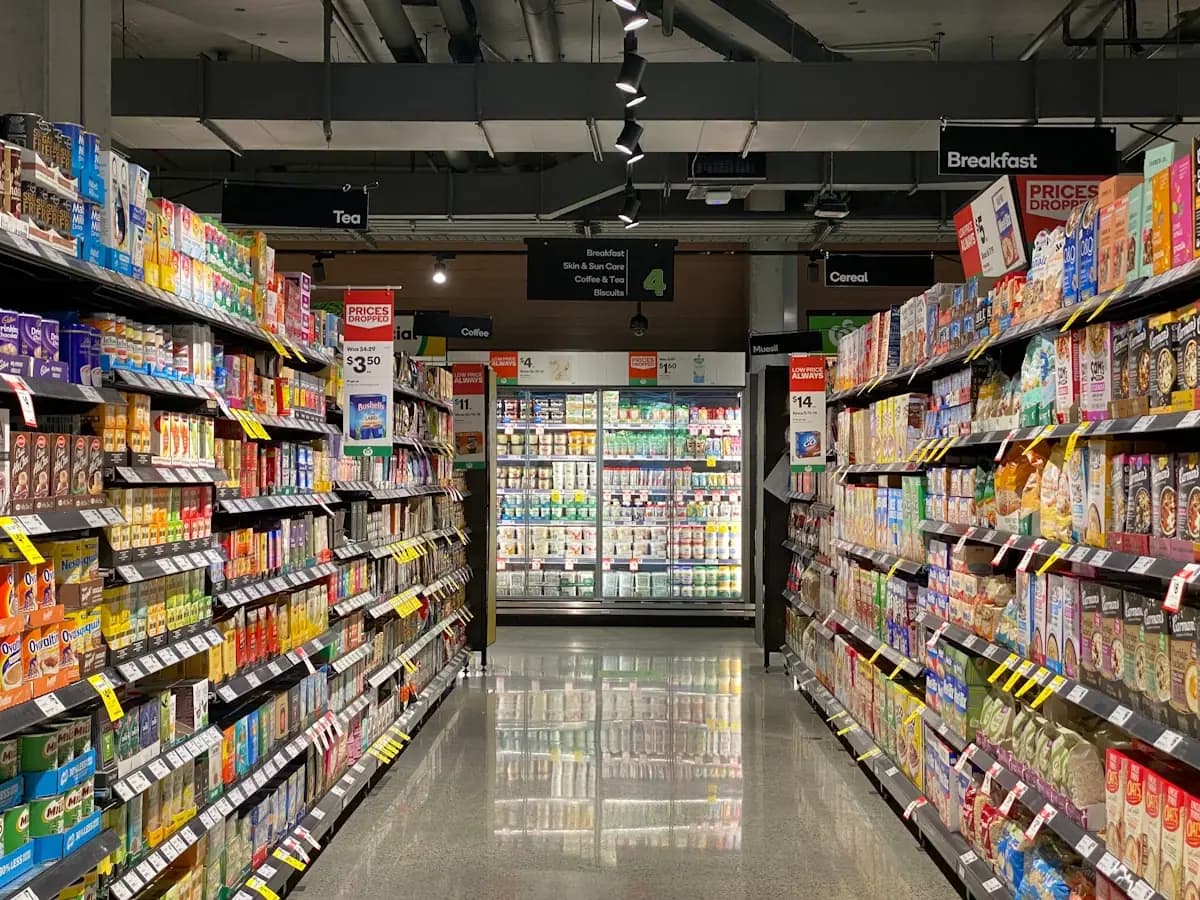 Modern grocery store aisle showing overhead category signs for Breakfast, Tea, and Cereal sections